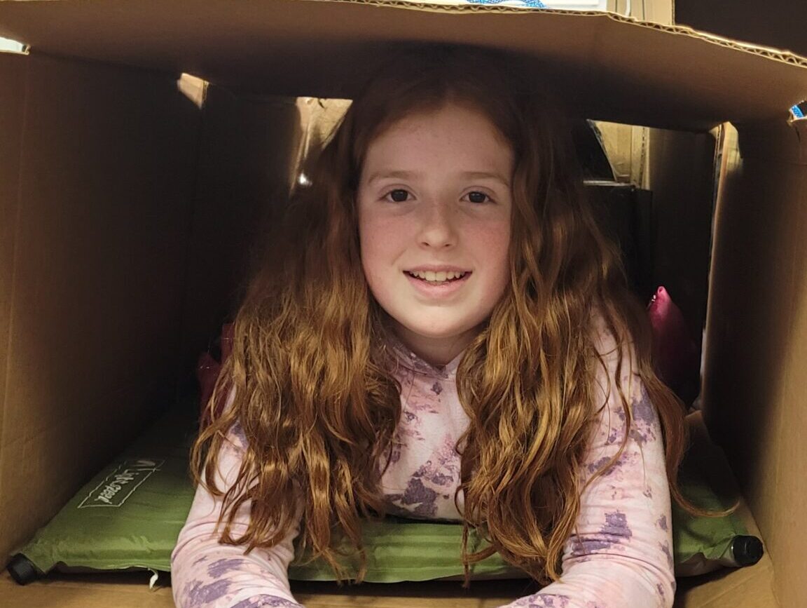 Girl laying down in her cardboard box shelter for night without a bed event