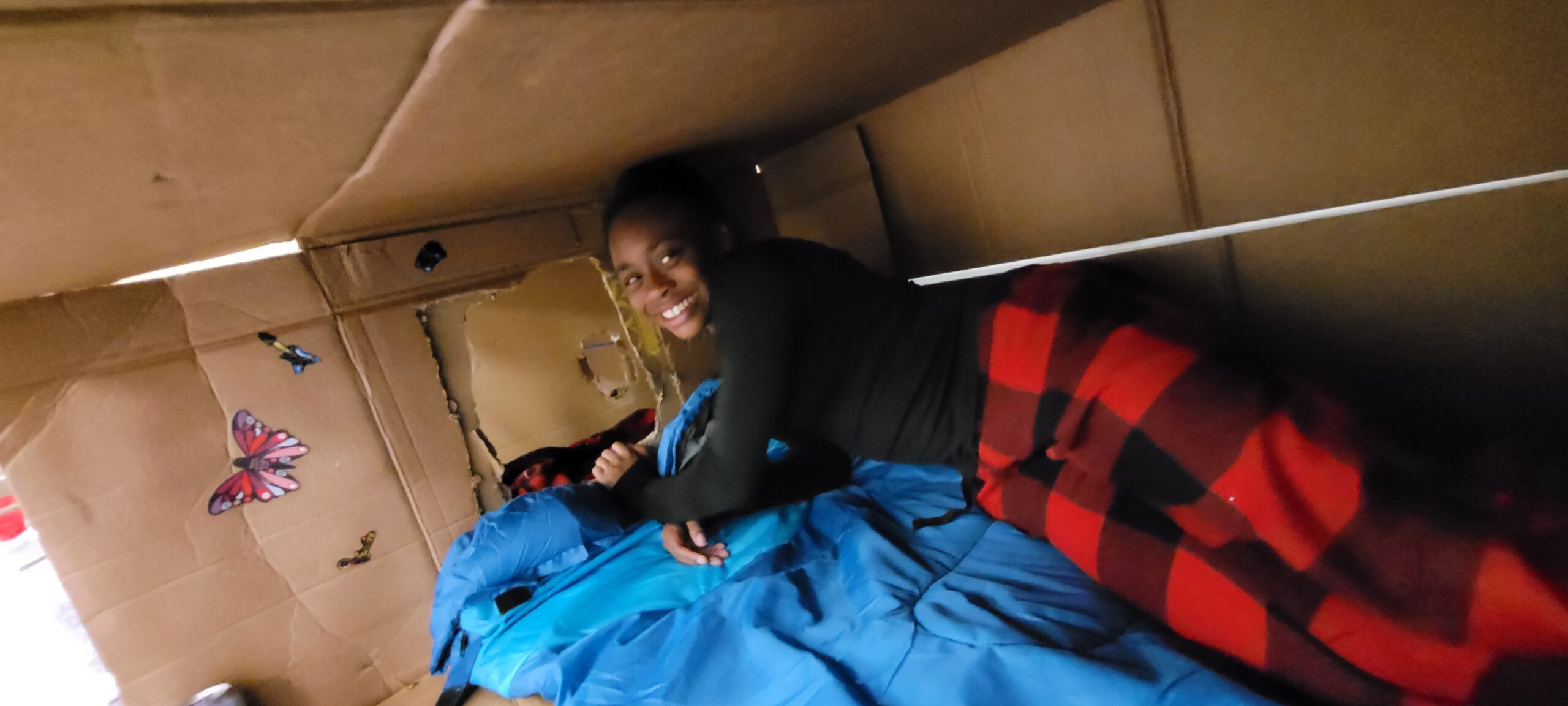 Young girl inside a cardboard box fort at the lunch break night without a bed event