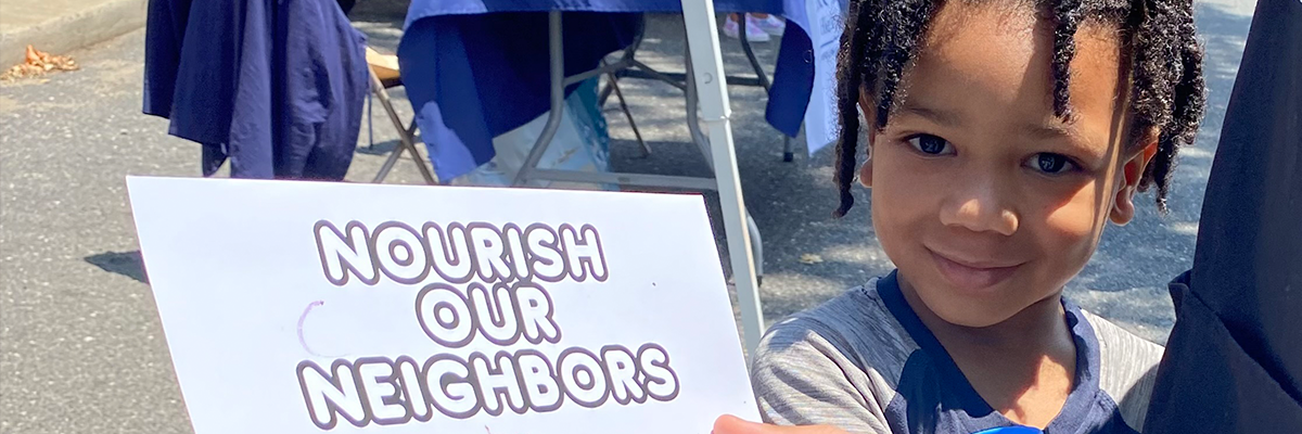 Child holding a sign that says "nourish our neighbors"